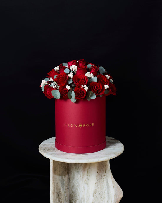 Red flower box with red roses and greenery on a dark background