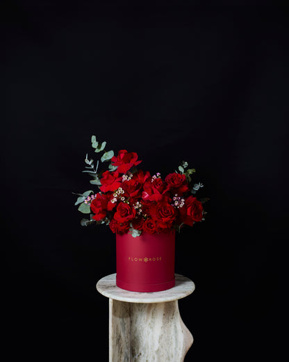 Red flowers in a red box on a wooden stand against a black background