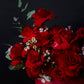 Bouquet of red roses with greenery in a red box against a black background